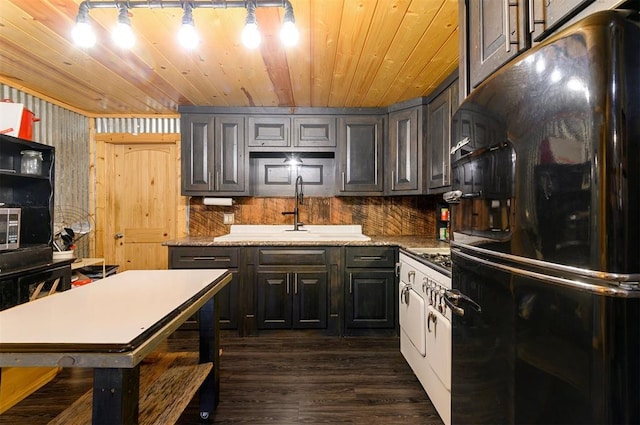 kitchen with black refrigerator, light stone counters, sink, and tasteful backsplash