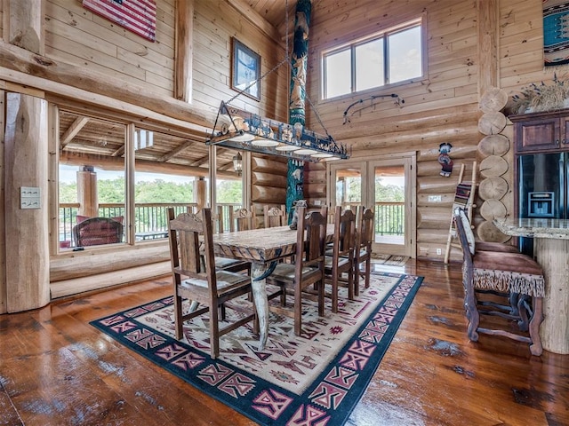 dining space with high vaulted ceiling, rustic walls, dark hardwood / wood-style flooring, and a healthy amount of sunlight