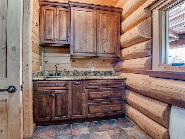 interior space with light stone countertops, sink, wood walls, and dark brown cabinetry