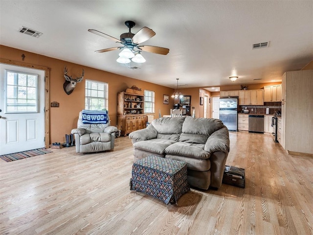 living room featuring ceiling fan with notable chandelier and light hardwood / wood-style floors