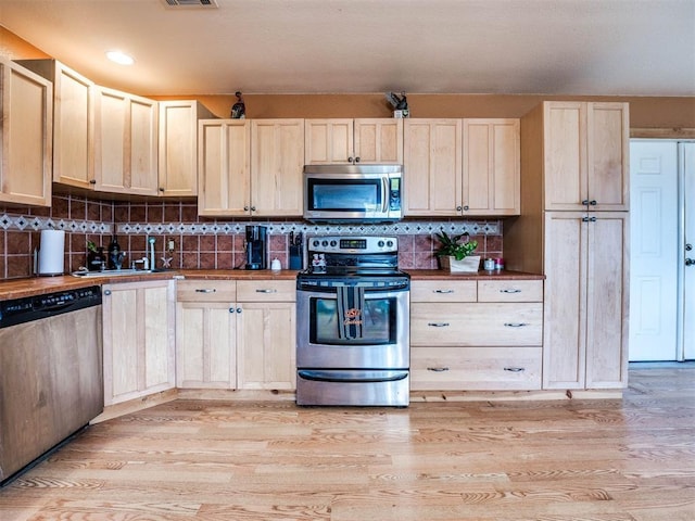 kitchen with decorative backsplash, appliances with stainless steel finishes, sink, and light hardwood / wood-style flooring