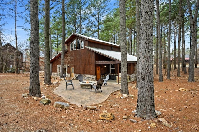 rear view of property featuring a fire pit, a patio area, and stone siding