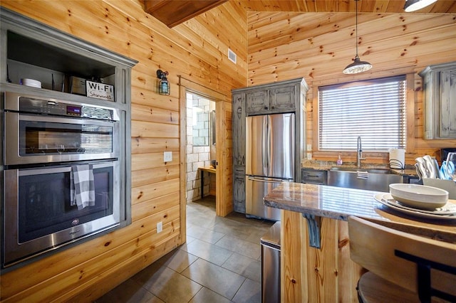 kitchen with appliances with stainless steel finishes, wooden walls, decorative light fixtures, high vaulted ceiling, and dark tile patterned flooring