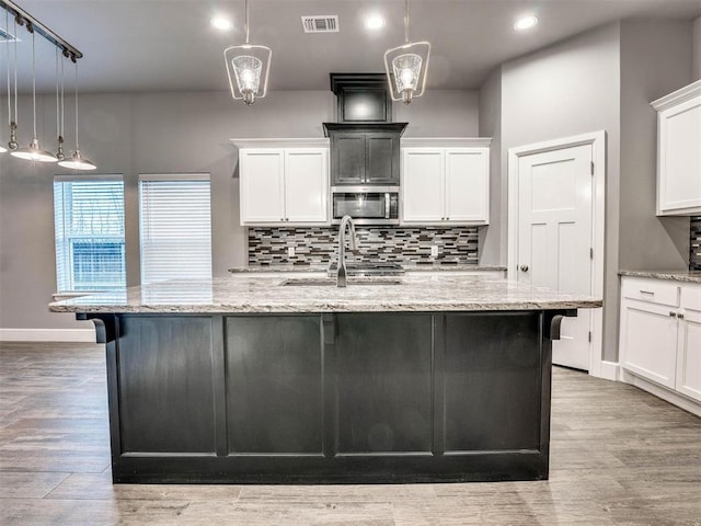 kitchen with light wood-type flooring, sink, decorative light fixtures, white cabinets, and a large island