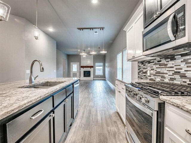 kitchen featuring white cabinetry, sink, hanging light fixtures, light stone counters, and appliances with stainless steel finishes