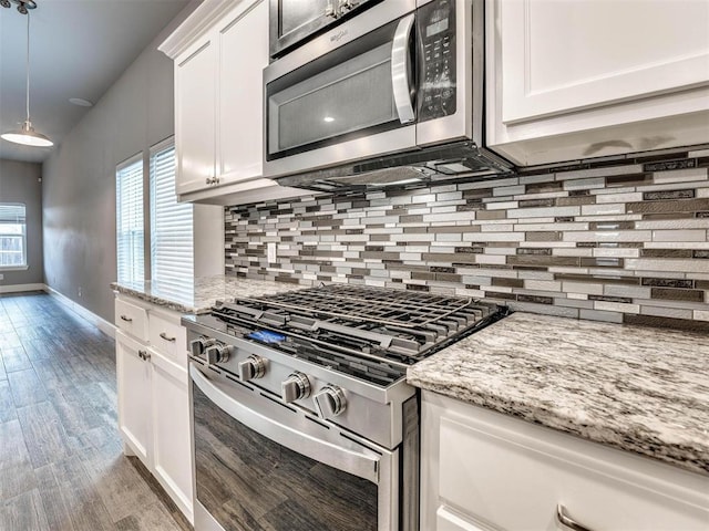 kitchen featuring tasteful backsplash, stainless steel appliances, pendant lighting, light hardwood / wood-style floors, and white cabinetry