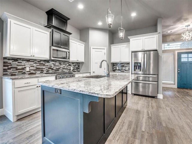 kitchen with pendant lighting, a kitchen island with sink, sink, appliances with stainless steel finishes, and white cabinetry