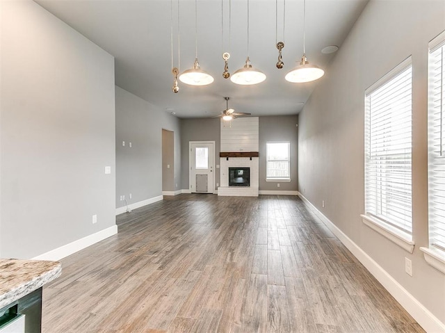 unfurnished living room with ceiling fan, wood-type flooring, and a brick fireplace