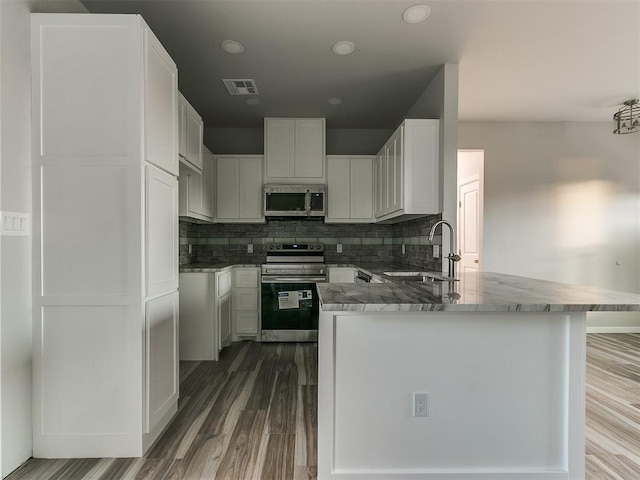 kitchen with sink, white cabinetry, appliances with stainless steel finishes, hardwood / wood-style floors, and decorative backsplash