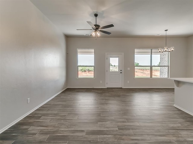 unfurnished living room with ceiling fan with notable chandelier and dark hardwood / wood-style flooring