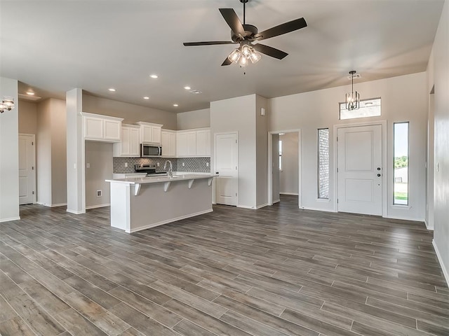 kitchen featuring white cabinetry, dark wood-type flooring, a center island with sink, ceiling fan with notable chandelier, and appliances with stainless steel finishes