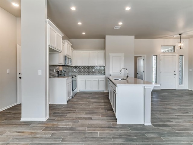 kitchen featuring stainless steel appliances, sink, hardwood / wood-style flooring, a center island with sink, and white cabinetry