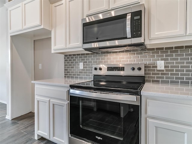 kitchen featuring light stone countertops, stainless steel appliances, tasteful backsplash, hardwood / wood-style floors, and white cabinets