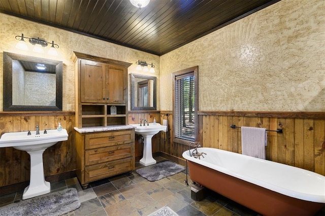 bathroom with dual sinks, a bath, wood ceiling, and wood walls