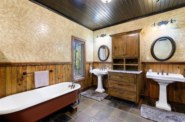 bathroom with double sink, wooden ceiling, a bath, and wooden walls