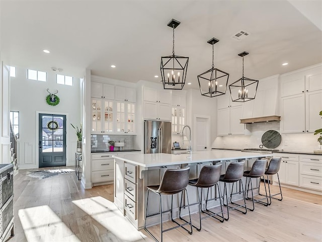 kitchen featuring a large island, a kitchen breakfast bar, stainless steel refrigerator with ice dispenser, white cabinets, and light wood-type flooring