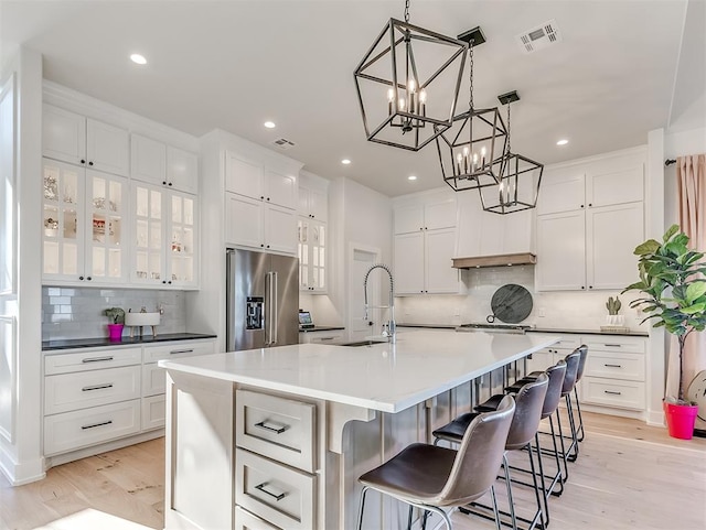 kitchen featuring light hardwood / wood-style flooring, a spacious island, decorative backsplash, white cabinets, and appliances with stainless steel finishes