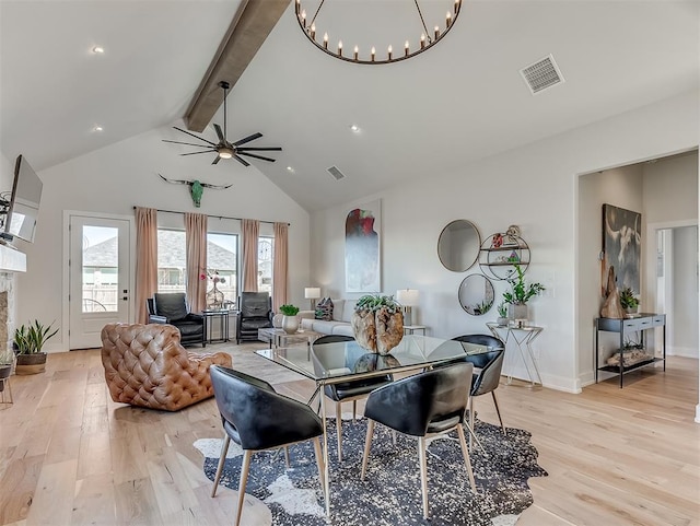 dining space with light wood-type flooring, a fireplace, ceiling fan with notable chandelier, high vaulted ceiling, and beamed ceiling