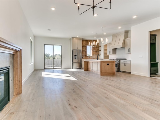 kitchen with a kitchen island with sink, hanging light fixtures, light hardwood / wood-style floors, custom range hood, and stainless steel appliances