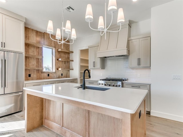 kitchen with a kitchen island with sink, sink, light hardwood / wood-style flooring, appliances with stainless steel finishes, and a notable chandelier