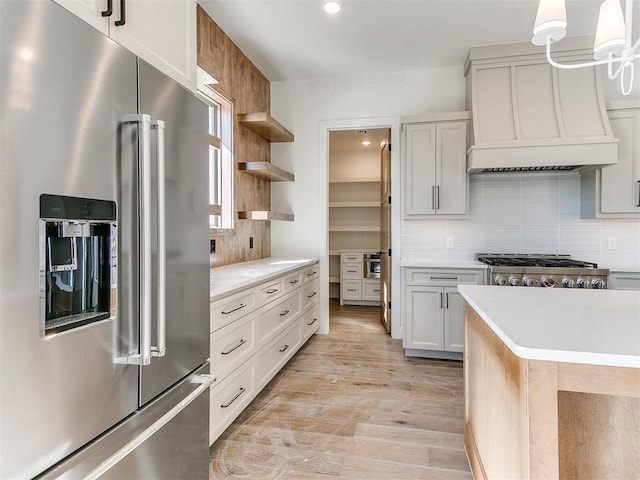 kitchen with custom range hood, stainless steel appliances, decorative light fixtures, light hardwood / wood-style floors, and white cabinetry