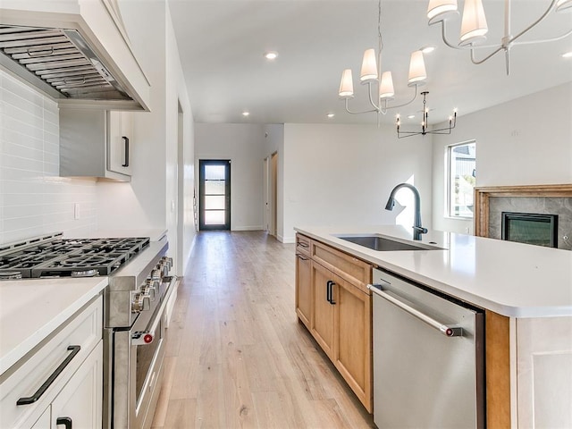 kitchen featuring custom exhaust hood, sink, appliances with stainless steel finishes, a notable chandelier, and light hardwood / wood-style floors