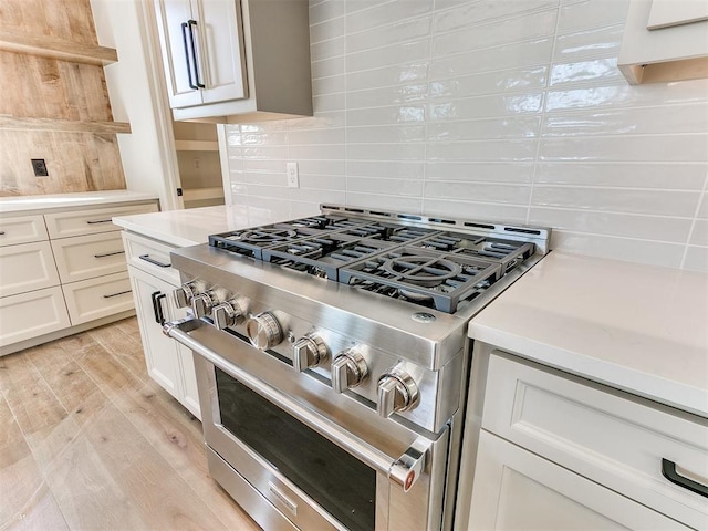 kitchen with white cabinetry, high end stove, backsplash, and light hardwood / wood-style flooring