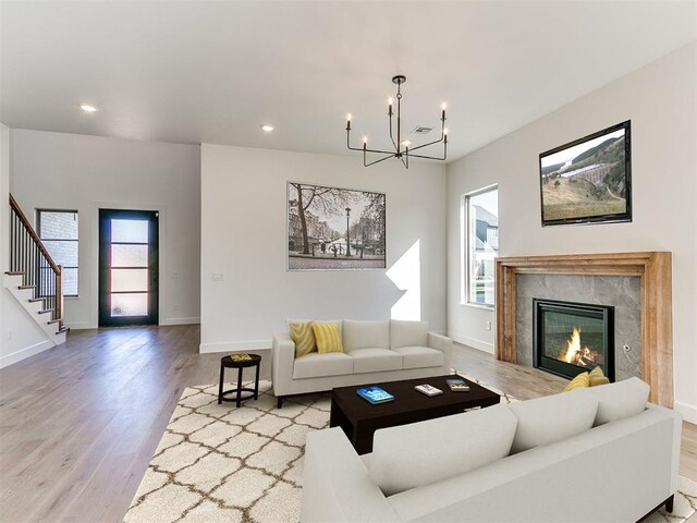 living room featuring light wood-type flooring, a high end fireplace, and an inviting chandelier