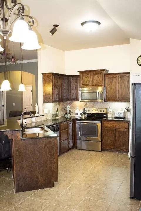 kitchen featuring sink, stainless steel appliances, kitchen peninsula, pendant lighting, and dark brown cabinets