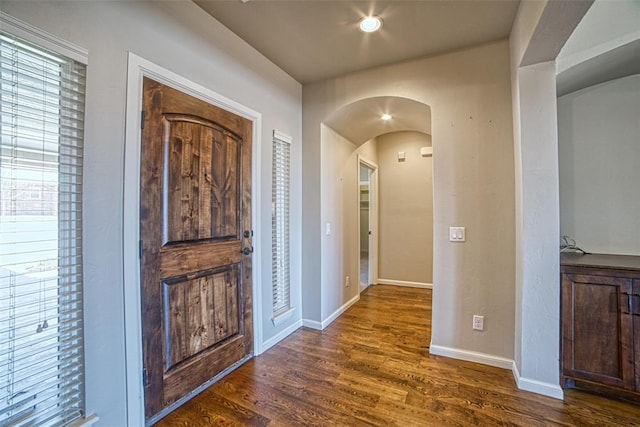 foyer with arched walkways, baseboards, and dark wood-type flooring