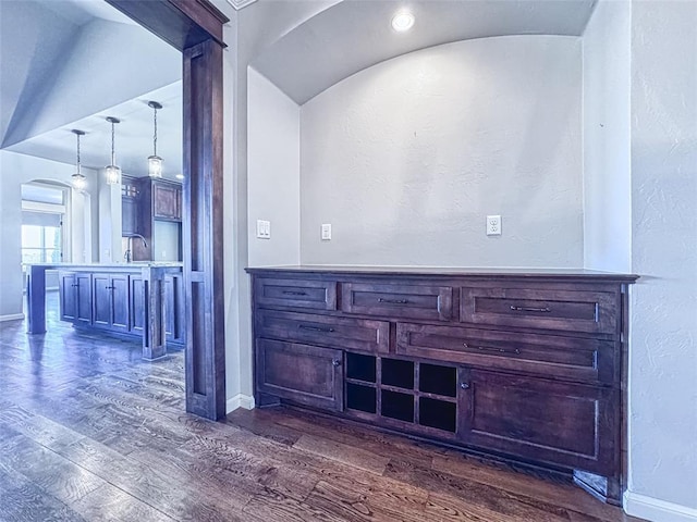 bar featuring dark wood-style floors, arched walkways, baseboards, lofted ceiling, and pendant lighting