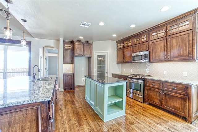 kitchen with visible vents, a sink, an island with sink, arched walkways, and appliances with stainless steel finishes