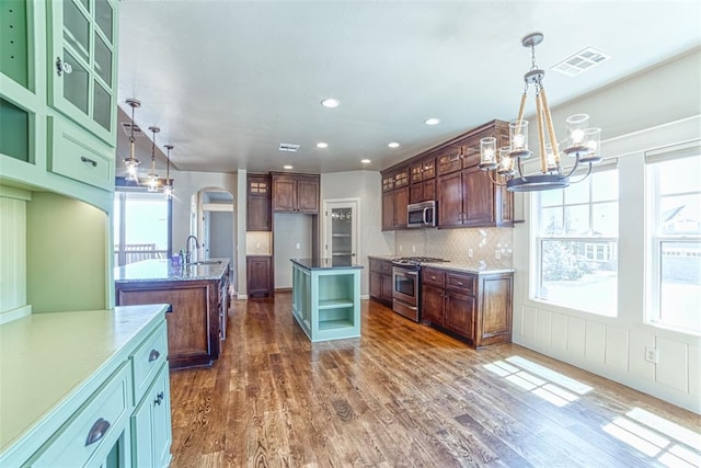 kitchen featuring a sink, a center island with sink, a chandelier, arched walkways, and appliances with stainless steel finishes