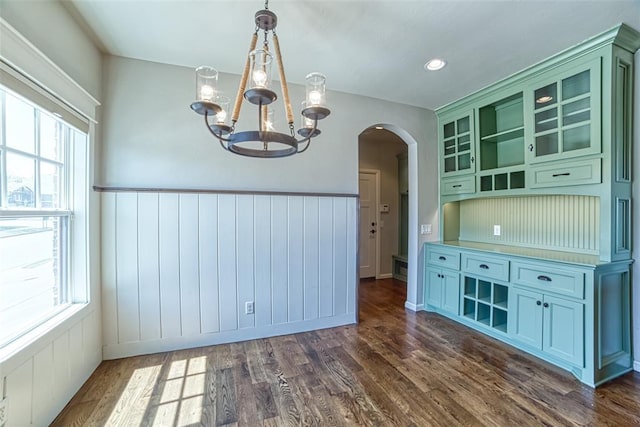 unfurnished dining area with dark wood-style flooring, arched walkways, a chandelier, and a wealth of natural light