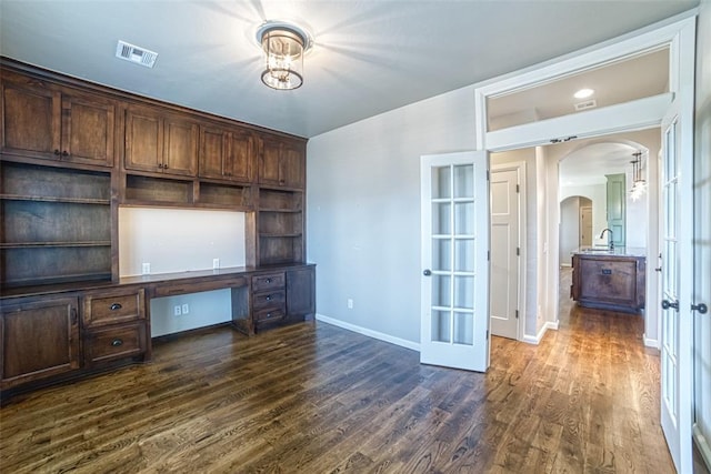 unfurnished office featuring french doors, visible vents, arched walkways, dark wood finished floors, and baseboards