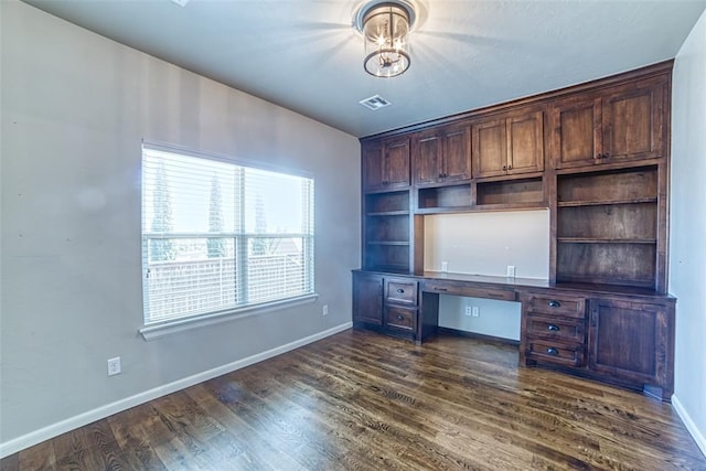 unfurnished office with dark wood-style flooring, baseboards, visible vents, and built in desk