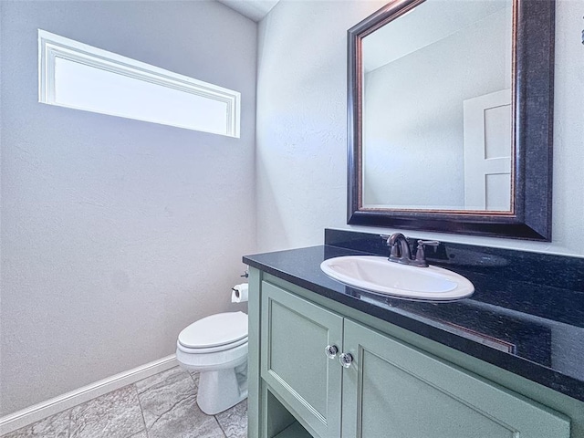 half bathroom featuring toilet, baseboards, and vanity