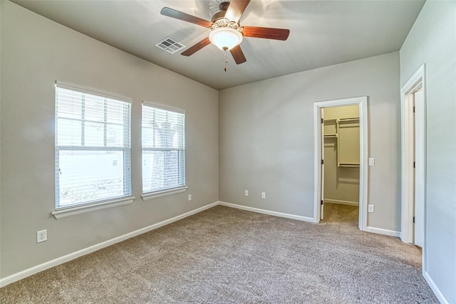unfurnished bedroom with visible vents, carpet, a walk in closet, and baseboards
