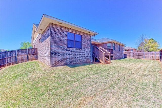 rear view of property featuring brick siding, a fenced backyard, a lawn, and stairs