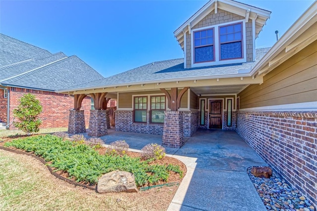 entrance to property featuring brick siding and a shingled roof