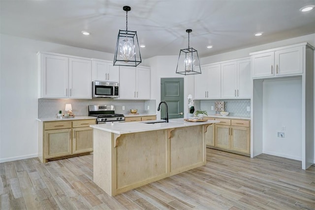 kitchen with appliances with stainless steel finishes, white cabinetry, sink, hanging light fixtures, and a center island with sink