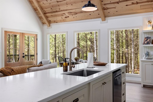 kitchen featuring sink, vaulted ceiling with beams, stainless steel dishwasher, pendant lighting, and light hardwood / wood-style floors