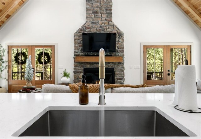 kitchen with french doors, beam ceiling, high vaulted ceiling, wooden ceiling, and a stone fireplace