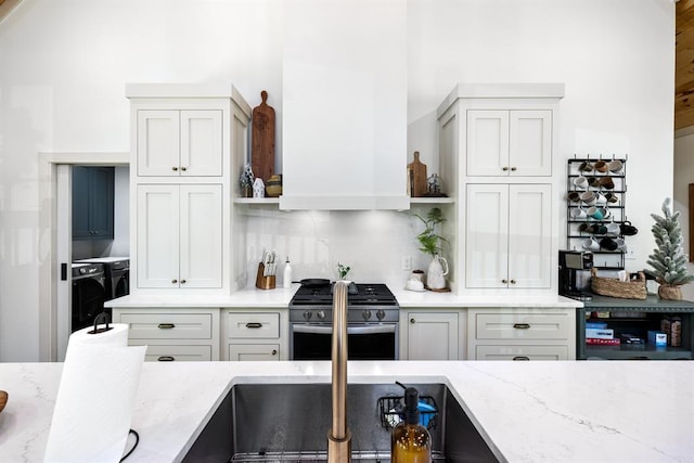 kitchen featuring separate washer and dryer, light stone counters, backsplash, extractor fan, and stainless steel range with gas stovetop