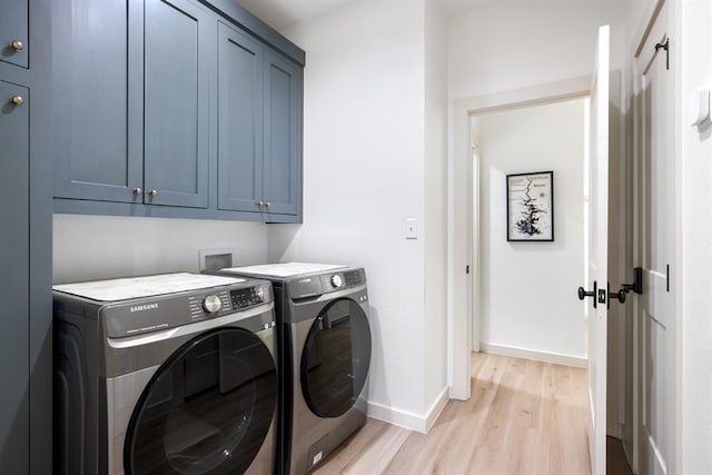 laundry room with cabinets, washing machine and dryer, and light hardwood / wood-style flooring