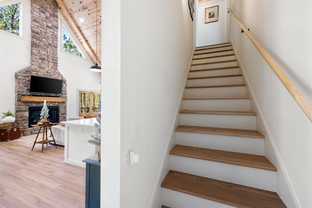 stairs featuring a fireplace, hardwood / wood-style floors, high vaulted ceiling, and wooden ceiling