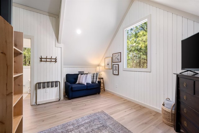 living area featuring lofted ceiling, wooden walls, and light hardwood / wood-style flooring