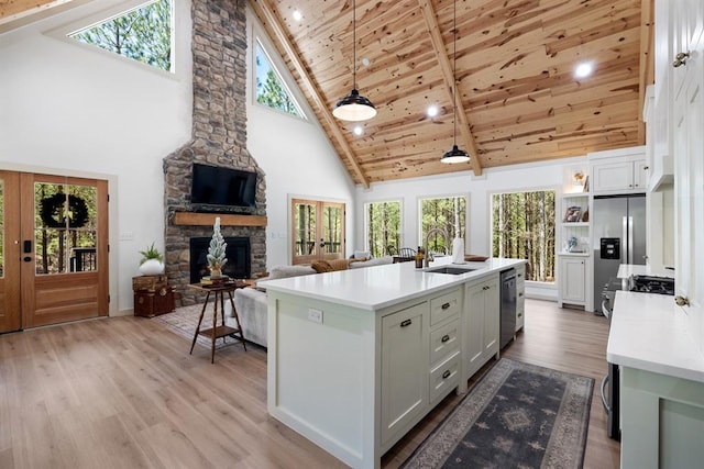 kitchen with sink, hanging light fixtures, appliances with stainless steel finishes, a kitchen island with sink, and white cabinets