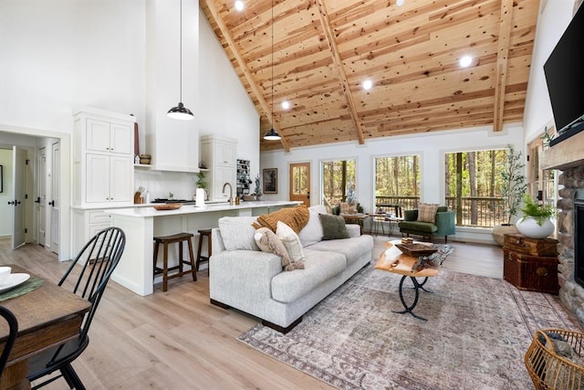 living room featuring high vaulted ceiling, a stone fireplace, wooden ceiling, and light wood-type flooring