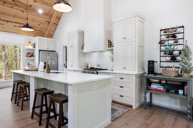 kitchen with sink, stainless steel refrigerator, a kitchen island with sink, white cabinets, and decorative light fixtures